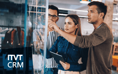 Three people collaborate in a modern office, pointing at a transparent board. The image is branded with the text “ITVT CRM” on the left side