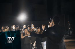 Ein Dirigent steht vor dem Publikum, den Taktstock in der Hand, und leitet leidenschaftlich das Orchester.