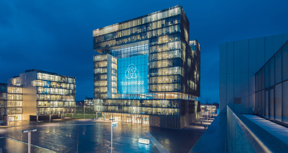 Moderne Bürogebäude bei Nacht mit beleuchteten Fenstern und einer großen Glasfassade, die