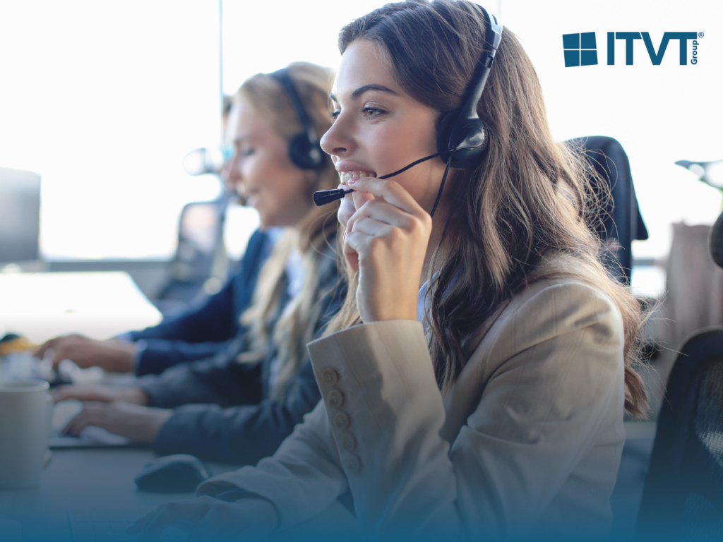 Drei Callcenter-Mitarbeiter mit Headsets, im Vordergrund eine lächelnde junge Frau, arbeiten an Computern. Das Logo der ITVT Group erscheint in der oberen rechten Ecke.